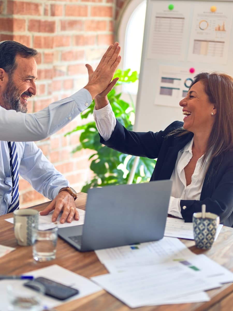 Two colleagues high-fiving across a desk after closing a deal